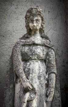 Statue of a beautiful woman with a sad expression. On background a gray and rough wall. Ideal for concepts and backgrounds.
