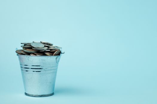 Full of money coins in a tin bucket on blue background for investment, business, finance and saving money concept 