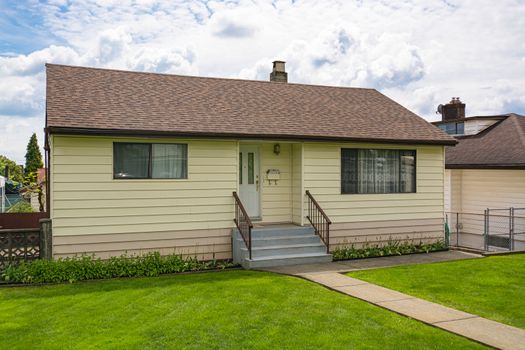 Modest family house with green lawn in front. Old residential house on cloudy day in Canada