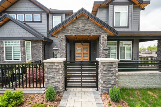 Entrance of luxury residential house with metal gate and stone texture walls. Big family house entrance with landscaped front yard