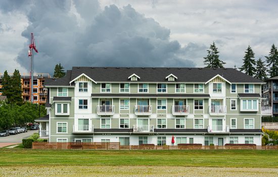 New residential low-rise building with big green lawn in front on cloudy sky background