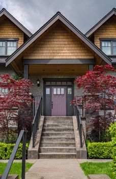 Entrance of luxury residential house with decorative red leave trees on site. Big family house entrance with landscaped front yard