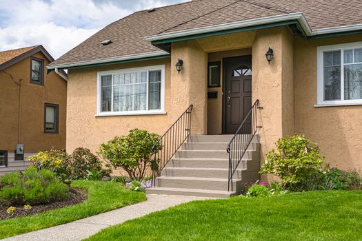 Entrance of average family house with green lawn in front. Residential house on cloudy day in Canada