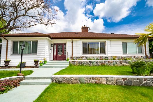 Family house with green lawn on land terraces. Average residential house on cloudy sky background