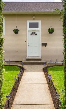 Back entrance of old family house with concrete pathway through green hedgerow fence