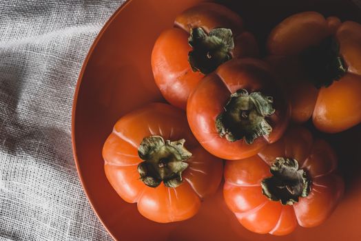 Few fresh persimmons on orange plate. View from above