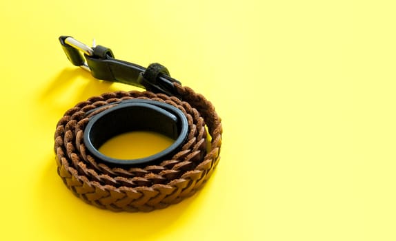 Brown woven leather braided belt isolated on yellow background.