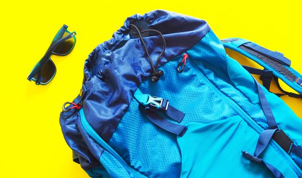 Large blue backpack and sun glasses. to travel trip isolated on yellow background.