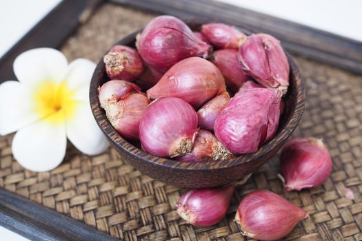 Red shallots in a bowl, placed on an old wooden tray bamboo weave.