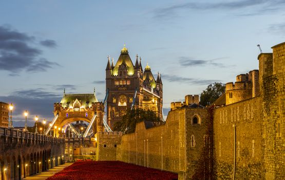 The walls of the famous Tower of London at night and the illuminated Tower Bridge in the background.