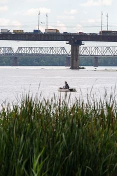 A fisherman on a boat on the Dnieper River in Kiev, Ukraine, close to the Pivnichnyi bridge (ex Moskovsky)