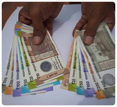 Man holding in two hand Indian new rupees currency spread from increasing order number and also like mirror image notes arranged with rupee coins in white paper