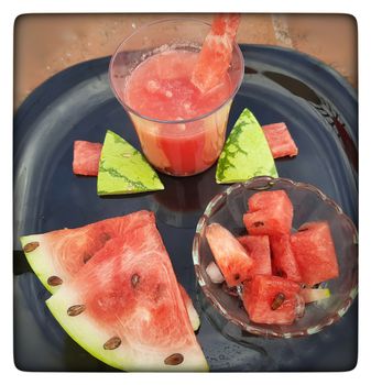 Chill watermelon juice with cut pieces and ice cubes with pieces in glass bowl and slices of watermelon in black plate and good for summer days and healthy fruit and also to keep body hydrate drink