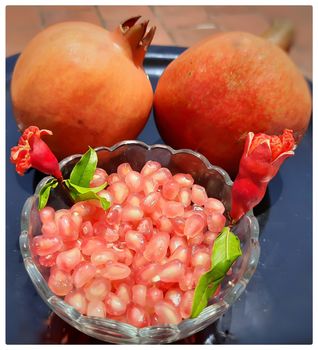 Two Pomegranate and Pomegranate seeds in bowl with shiny red “jewels” inside and its flower buds kept in bowl and placed beautifully in black plate