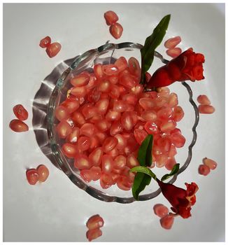 Pomegranate seeds in bowl with shiny red “jewels” inside and its flower buds kept in bowl and placed beautifully in white plate