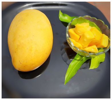 Yellow tasty mango with cut pieces in bowl and slice designed beautifully in black plate with its leaves and summer fruit and good for health also