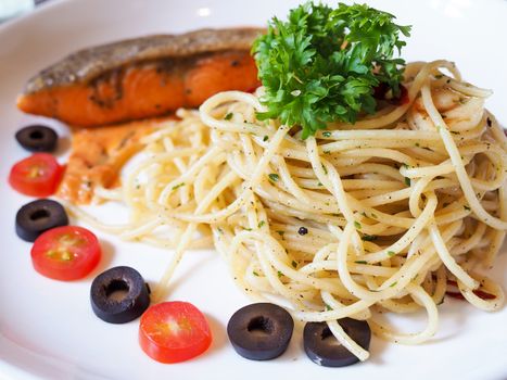 pasta spaghetti with grilled salmon and dill in white plate on food table.