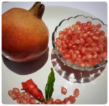 Two Pomegranate and Pomegranate seeds in bowl with shiny red “jewels” inside and its flower buds kept in bowl and placed beautifully in white plate