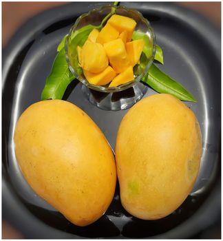 Yellow two tasty mango with cut pieces in bowl kept beautifully in black plate and summer fruit and good for health also