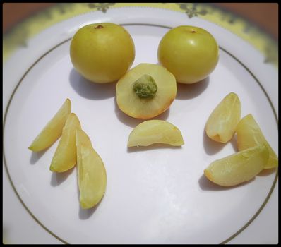 Colorful yellow healthy Gooseberry and its pieces arranged beautifully in white plate and it is rich in fiber control blood sugar good for heart and healthy diet and also rich in Vitamin C