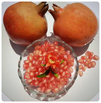 Two Pomegranate and Pomegranate seeds in bowl with shiny red “jewels” inside and its flower buds kept in bowl and placed beautifully in white plate