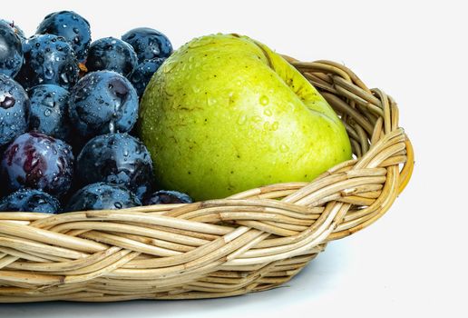 Bright purple grapes and green apples in a wooden basket on a white background.