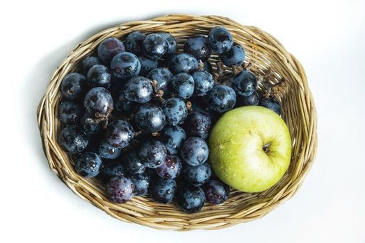 Bright purple grapes and green apples in a wooden basket on a white background.