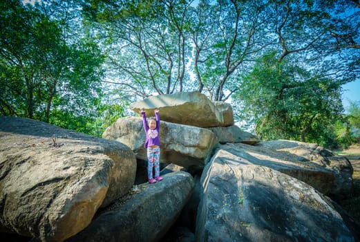 little girl standing with raised hands on rock and tree background