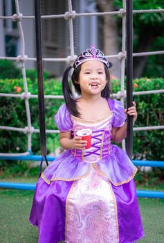 Portrait of cute smiling little girl in princess costume eating snack on swing