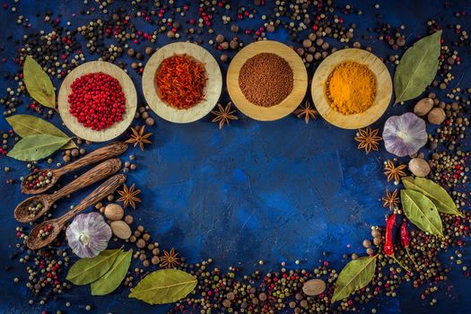 Spicy background with copy space. Assorted spices on a dark blue background. Concept- Cooking at home. Curry, saffron, pink peppercorns, star anise, hot chili, garlic, bay leaf, nutmeg. Top view, close up.