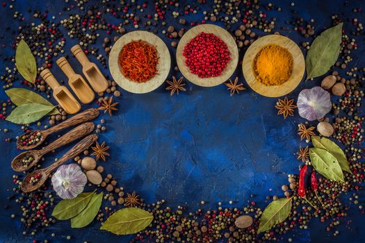 Assorted spices in the wooden bowls with spoons on a dark blue background. Spices concept- Cooking at home. Curry, saffron, pink peppercorns, star anise, hot chili, garlic, bay leaf, nutmeg. Top view.  Copy space.