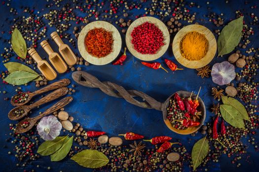 Various fragrant spices and herbs on a dark blue background. Spicy background with pepper mix and other spices. Colorful spices for cooking with vintage handmade wooden spoon. Top view, flat-lay.