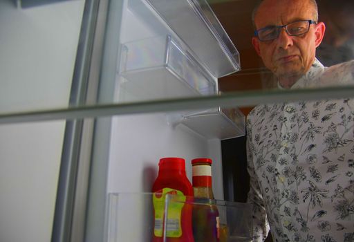 Hungry man opening and looking for food in refrigerator, at the empty refrigerator. Senior man looking for a snack in the fridge at night, view from the fridge.