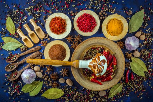 Various fragrant spices on a dark blue background. Vintage pestle and mortar with assortment of pepper mix and hot chili. Various spices inspiring our recipes while we cook at home.  Top view. Flat-lay.