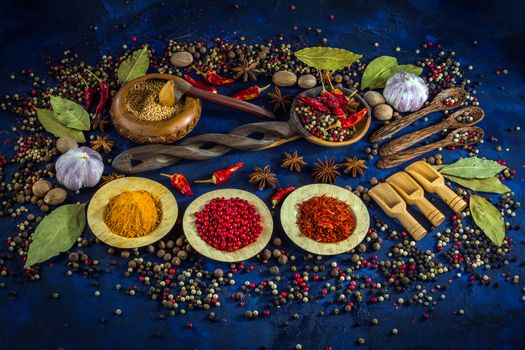 Various fragrant spices and herbs on a dark blue background. Spicy background with pepper mix and other spices. Colorful spices for cooking with vintage handmade wooden spoon and bowl. Top view, flat-lay.