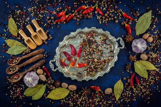 Various spices and wooden spoons on a dark blue background. Spicy background with pepper mix on a vintage silver plated tray.  Spices concept- Cooking at home. Top view, close up, flat-lay.