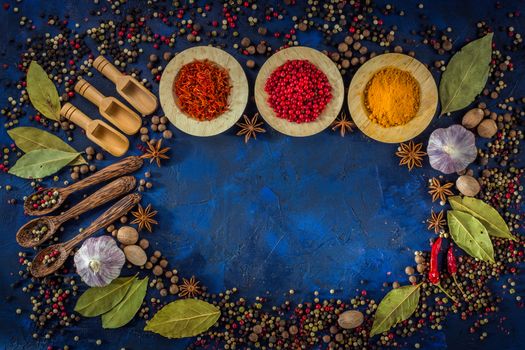 Various spices in bowls and wooden spoons on a dark blue background. Asian spices concept. Assorted aromatic ingredients. Natural food additives with copy space. Top view, close up, flat-lay. Copy space.