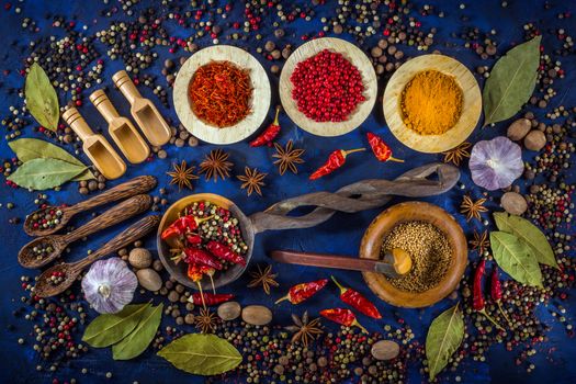 Various fragrant spices and herbs on a dark blue background. Spicy background with pepper mix and other spices. Colorful spices for cooking with vintage handmade wooden spoon and bowl. Top view, flat-lay.