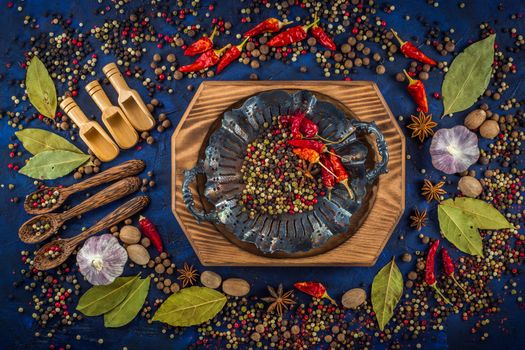 Assortment of colorful spices on a dark blue background. Spicy background with pepper mix on a vintage silver plate. Various spices, star anise, pepper, hot chili, garlic, bay leaf, nutmeg. Top view, flat-lay.