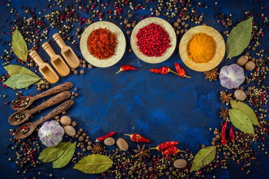 Assorted spices in the wooden bowls with spoons on a dark blue background. Spices concept- Cooking at home. Curry, saffron, pink peppercorns, star anise, hot chili, garlic, bay leaf, nutmeg. Top view.  Copy space.