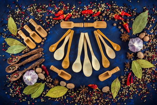 Various spices and wooden spoons on a dark blue background. Cooking at home. Colorful spices for cooking with handmade wooden spoon. Top view, flat-lay.