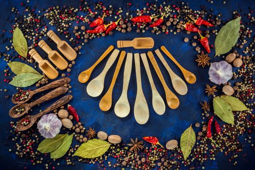 Various spices and wooden spoons on a dark blue background. Colorful spices for cooking with vintage handmade wooden spoon. Pepper mix, star anise, hot chili, garlic, bay leaf, nutmeg. Top view, flat-lay.