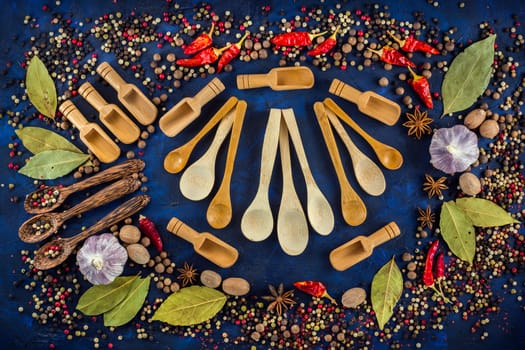 Various spices and wooden spoons on a dark blue background. Spicy background concept with various wooden spoons. Cooking at home. Top view, close up, flat-lay.