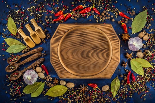 Various fragrant spices and herbs on a dark blue background. Spicy background with pepper mix and other spices. Colorful spices for cooking with vintage handmade wooden spoon and bowl. Top view, flat-lay.