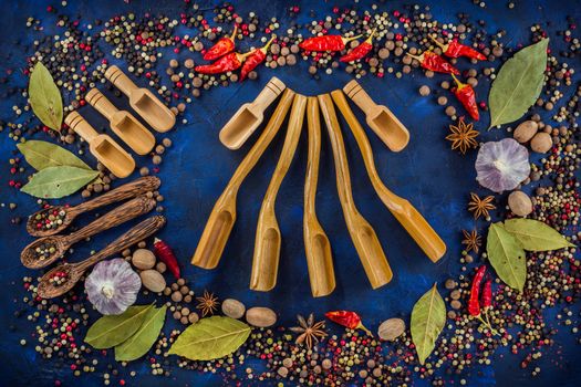 Various spices and wooden spoons on a dark blue background. Cooking at home. Colorful spices for cooking with handmade wooden spoon. Top view, flat-lay.