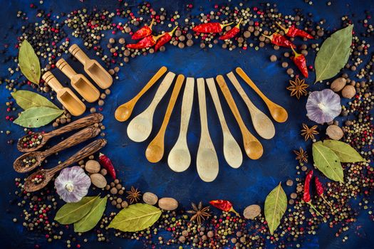 Various spices and wooden spoons on a dark blue background. Assorted aromatic ingredients. Colorful spices for cooking with handmade wooden spoon. Top view, flat-lay.