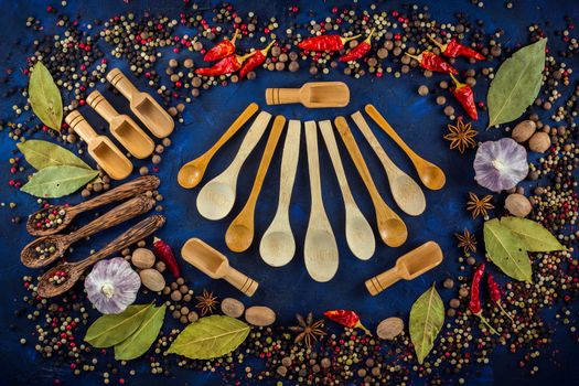 Assorted spices on a dark blue background. Spices concept with various wooden spoons. Assorted aromatic ingredients, pepper mix, star anise, hot chili, garlic, bay leaf, nutmeg. Top view, close up, flat-lay.