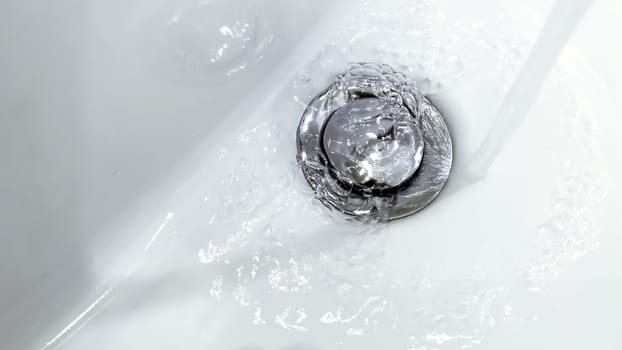 water falling from a tap into a white ceramic sink with a metal strainer