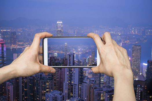 Girl taking pictures on mobile smart phone in HongKong cityscape at night , Hong kong city.