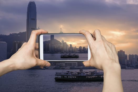 Girl taking pictures on mobile smart phone in Hong Kong's Victoria Harbour in sunrise